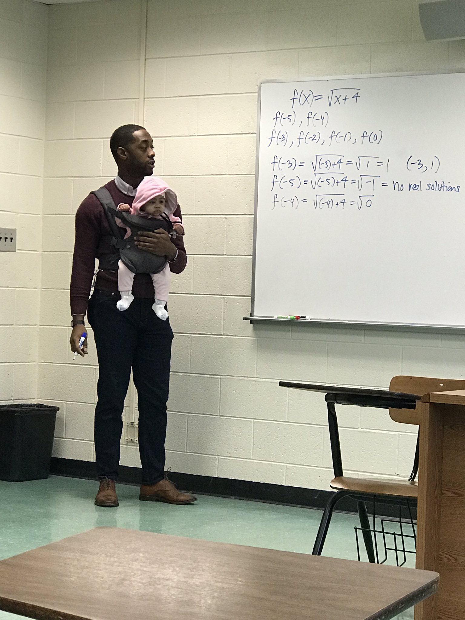 Un professeur porte le bébé d'un de ses élèves pour qu'il puisse prendre des notes