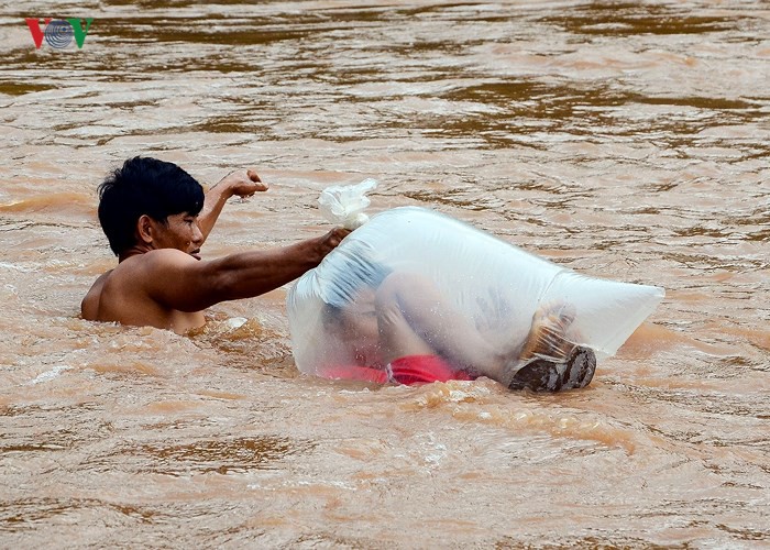 Pour rester au sec, un écolier vietnamien traverse une rivière dans un sac plastique